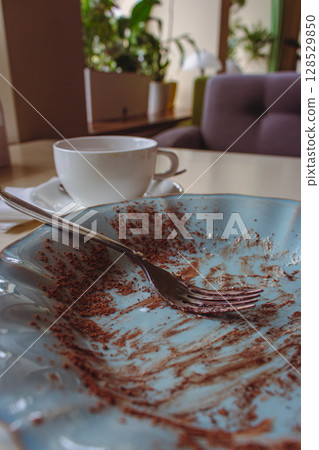 Empty blue vintage plate with white cup in restaurant. Dirty plate with fork after eating chocolate cake. After dessert flat lay. Sweet food concept. Italian dessert. Breakfast in cafe. Empty blue vintage plate with white cup in restaurant. Dirty plate with fork after eating chocolate cake. After dessert flat lay. Sweet food concept. Italian dessert. Breakfast in cafe. 128529850