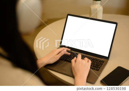 Close up of woman typing on laptop with blank white screen at a cafe table 128530198