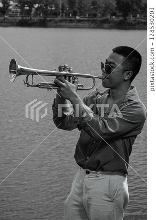Portrait of trumpet player outdoors with calm lake as the background in monochrome style 128530201