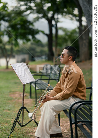 Trumpet player resting on bench with music stand, enjoying a quiet outdoor practice session 128530205