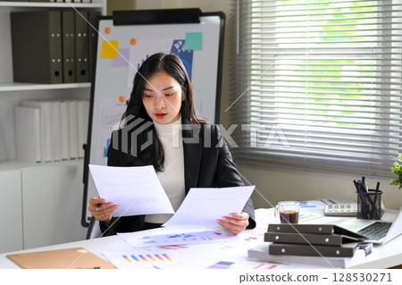 Focused female executive analyzing financial reports at bright office 128530271