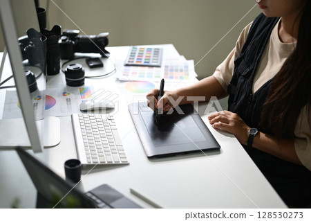 Photographer retouching images on a graphic tablet at a workstation 128530273