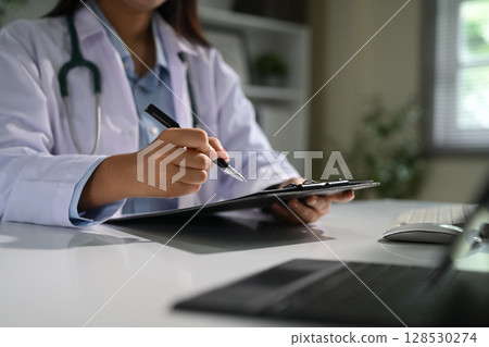 Close up of female doctor filling out patient information or notes during consultation online Close up of female doctor filling out patient information or notes during consultation online 128530274