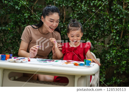 happy mother and toddler girl painting watercolor in paper at backyard. 128530513