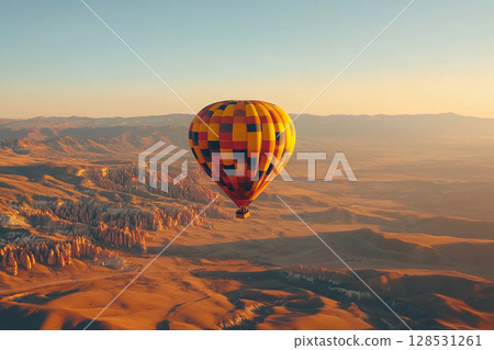 Hot air balloon flying over desert dunes at sunrise with warm glowing sky and peaceful atmosphere Hot air balloon flying over desert dunes at sunrise with warm glowing sky and peaceful atmosphere 128531261