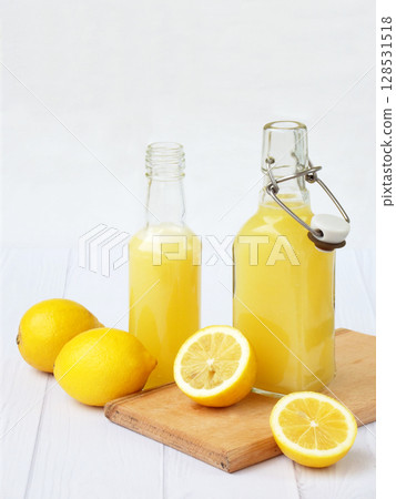 Freshly squeezed lemon juice in bottle and lemons on light background. For vitamin drink or cocktail. Selective focus. Space for text 128531518
