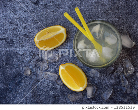 One glass of cold homemade lemonade with lemon slices, ice cubes and straws on dark background. Copy space 128531539