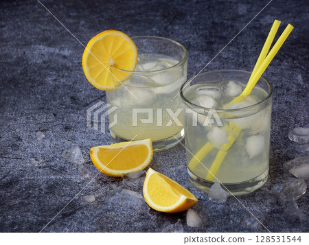 glasses of cold homemade lemonade with lemon slices, ice cubes and straws on dark background. Copy space. 128531544