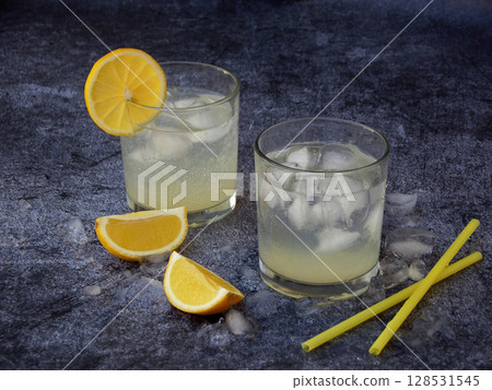 glasses of cold homemade lemonade with lemon slices, ice cubes and straws on dark background. Copy space glasses of cold homemade lemonade with lemon slices, ice cubes and straws on dark background. Copy space 128531545