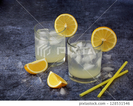 Two glasses of cold homemade lemonade with lemon slices, ice cubes and straws on dark background. Copy space 128531546