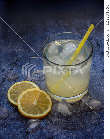 One glass of cold homemade lemonade with lemon slices, ice cubes and straws on dark background. Copy space 128531550
