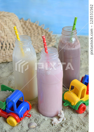 Three bottle of various milkshakes chocolate, strawberry and vanilla . Healthy smoothie with straw. Tasty milk shake cocktails. Refreshing summer drink on yellow sand summer beach. Copy space 128531562