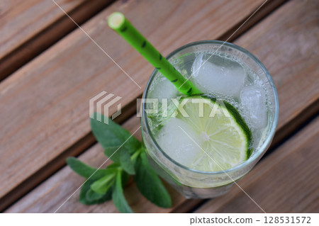 Glass of cold homemade lemonade or mojito cocktail with lime and mint on wooden background. Soda drink. Copy space Glass of cold homemade lemonade or mojito cocktail with lime and mint on wooden background. Soda drink. Copy space 128531572