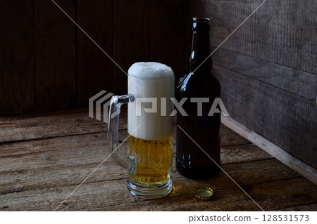 Mug of beer, bottle on wooden background. Photographed with natural light Mug of beer, bottle on wooden background. Photographed with natural light 128531573