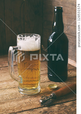 Mug of beer, bottle on wooden background. Photographed with natural light Mug of beer, bottle on wooden background. Photographed with natural light 128531574