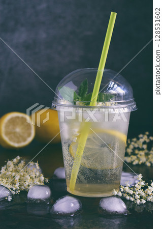 Homemade elderflower lemonade with lemon and elderberry flowers in plastic cup with sphere dome cap and cocktail tube. Elderflower cordial. Summer cold drink 128531602