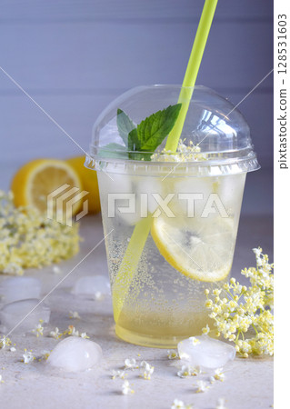 Homemade elderflower lemonade with lemon and elderberry flowers in plastic cup with sphere dome cap and cocktail tube. Elderflower cordial. Summer cold drink. 128531603