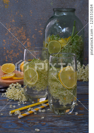 Elderberry flowers and lemon drink. Refreshing healthy summer juice. Glass of elderflower lemonade on wooden rustic board. Alternative medicine and therapy. 128531684