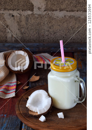 Coconut milk in bottle with broken coco on wooden background. Delicious milk cocktail. Copy space Coconut milk in bottle with broken coco on wooden background. Delicious milk cocktail. Copy space 128531694