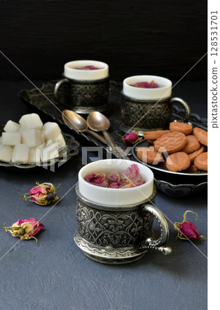 Floral tea made from rose petals and cookies on a dark gray concrete background. Tea drinking in eastern style. 128531701