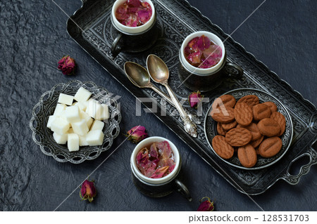 Floral tea made from rose petals and cookies on a dark gray concrete background. Tea drinking in eastern style. Romantic breakfast for Valentine's Day, Women's Day, Mother's Day 128531703