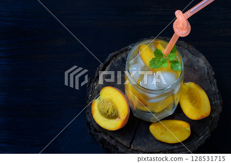 Glass of cold homemade peach lemonade or mojito cocktail with mint on dark background. Soda drink. Copy space. Photographing with natural light Glass of cold homemade peach lemonade or mojito cocktail with mint on dark background. Soda drink. Copy space. Photographing with natural light 128531715