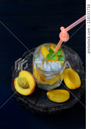 Glass of cold homemade peach lemonade or mojito cocktail with mint on dark background. Soda drink. Copy space. Photographing with natural light Glass of cold homemade peach lemonade or mojito cocktail with mint on dark background. Soda drink. Copy space. Photographing with natural light 128531716