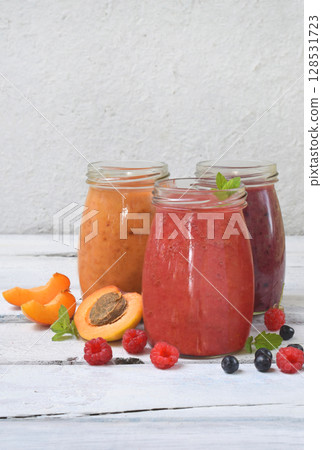 Orange, red and purple healthy smoothies of fresh ingredients - bananas, apricots, raspberries and blueberries on a light background. Copy space 128531723