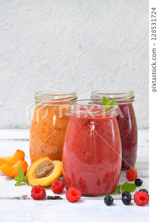 Orange, red and purple smoothies of fresh ingredients - bananas, apricots, raspberries and blueberries on a light background. Healthy food concept. Vegetarian product. Organic Raw Drink. Copy space. Orange, red and purple smoothies of fresh ingredients - bananas, apricots, raspberries and blueberries on a light background. Healthy food concept. Vegetarian product. Organic Raw Drink. Copy space. 128531724