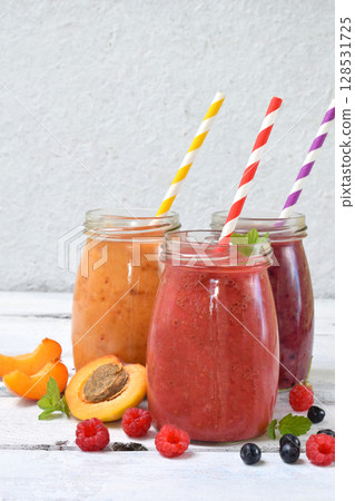 Orange, red and purple healthy smoothies of fresh ingredients - bananas, apricots, raspberries and blueberries on a light background. Copy space 128531725
