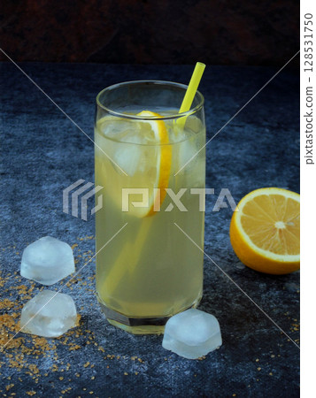 One glass of cold homemade lemonade with lemon slices, ice cubes, brown sugar and straws on dark background. Copy space One glass of cold homemade lemonade with lemon slices, ice cubes, brown sugar and straws on dark background. Copy space 128531750