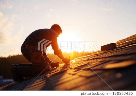 A close-up image of a home repair, focusing on a roofer installing shingles on a roof. 128533430