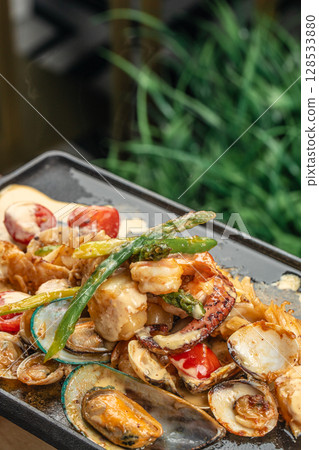 A sizzling seafood medley with shrimp, mussels, clams, and vegetables served hot on a black grill plate with creamy sauce and herbs A sizzling seafood medley with shrimp, mussels, clams, and vegetables served hot on a black grill plate with creamy sauce and herbs 128533880