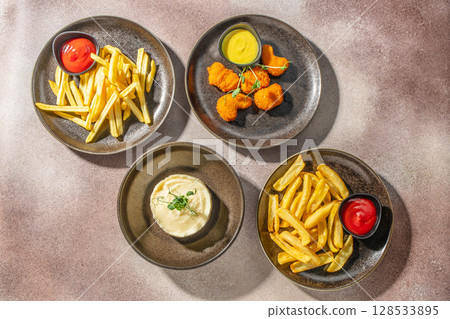Assorted comfort food dishes including French fries, chicken nuggets with mustard sauce, and mashed potatoes served on rustic plates Assorted comfort food dishes including French fries, chicken nuggets with mustard sauce, and mashed potatoes served on rustic plates 128533895