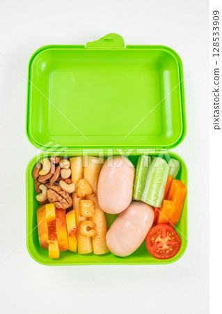 Bright green lunchbox filled with sausages, cheese, nuts, fruits, and fresh vegetables including cucumber, carrot, and tomato, organized in a colorful and nutritious arrangement Bright green lunchbox filled with sausages, cheese, nuts, fruits, and fresh vegetables including cucumber, carrot, and tomato, organized in a colorful and nutritious arrangement 128533909