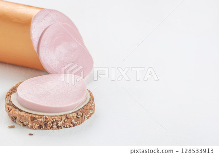 Close-up of a slice of pink bologna sausage on whole grain bread with sesame seeds, set on a clean white background. top view. copy space 128533913