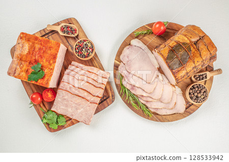 A delicious assortment of smoked and cooked meats is beautifully arranged on wooden boards with herbs, spices, and fresh vegetables, ideal for showcasing traditional deli or charcuterie products A delicious assortment of smoked and cooked meats is beautifully arranged on wooden boards with herbs, spices, and fresh vegetables, ideal for showcasing traditional deli or charcuterie products 128533942