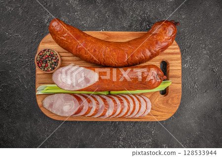 Smoked pork sausages sliced and served on a wooden cutting board with green onion and a bowl of mixed peppercorns on a dark textured background Smoked pork sausages sliced and served on a wooden cutting board with green onion and a bowl of mixed peppercorns on a dark textured background 128533944
