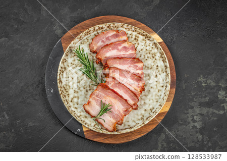 Sliced smoked pork belly arranged on a speckled ceramic plate with fresh rosemary garnish, showcasing rich marbling and savory crust Sliced smoked pork belly arranged on a speckled ceramic plate with fresh rosemary garnish, showcasing rich marbling and savory crust 128533987