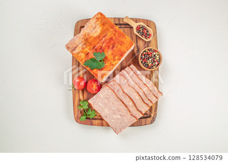 Sliced ham loaf is displayed on a wooden board with whole and halved cherry tomatoes, parsley, and colorful peppercorns, creating a simple and appetizing presentation 128534079