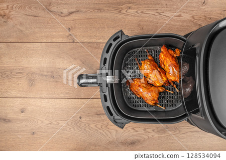 Three perfectly roasted quails with golden, crispy skin are arranged inside an air fryer basket, ready to serve on a wooden background 128534094