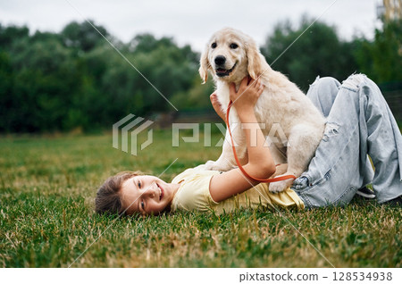 On the ground. Cute little girl is with golden retriever dog on the field On the ground. Cute little girl is with golden retriever dog on the field 128534938