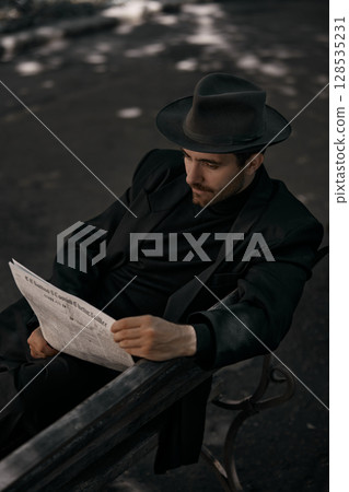 Individual in hat reads newspaper on park bench in speckled light 128535231