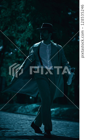 Mysterious figure in vintage attire walking in moonlit street at night Mysterious figure in vintage attire walking in moonlit street at night 128535246