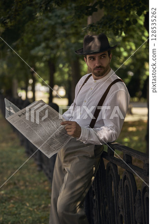 Gentleman in retro clothing reads newspaper outside in speckled sunlight Gentleman in retro clothing reads newspaper outside in speckled sunlight 128535262