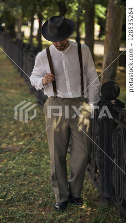 Man walking in vintage attire along park fence on sunny day 128535264