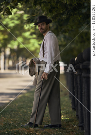 Man in vintage attire walking on tree-lined street under sunlight Man in vintage attire walking on tree-lined street under sunlight 128535265