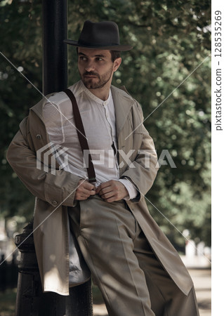 Man in vintage attire leaning casually against lamppost outdoors Man in vintage attire leaning casually against lamppost outdoors 128535269