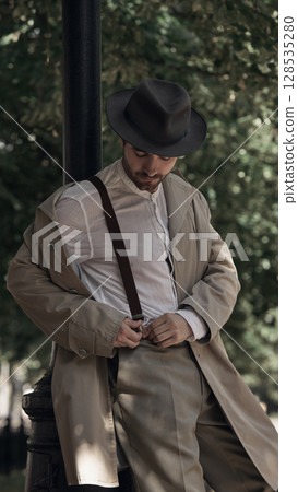 Man in vintage clothing adjusting suspenders outdoors in park Man in vintage clothing adjusting suspenders outdoors in park 128535280