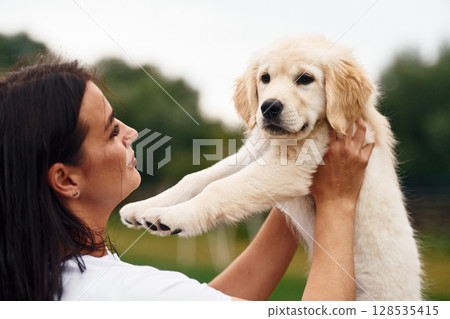 Cute little dog. Woman with golden retriever dog is on the green field Cute little dog. Woman with golden retriever dog is on the green field 128535415
